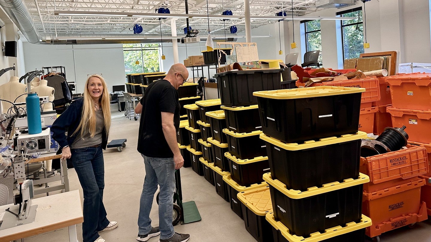 Two UO Portland employees looking at stacked storage bins in a large open space inside a building